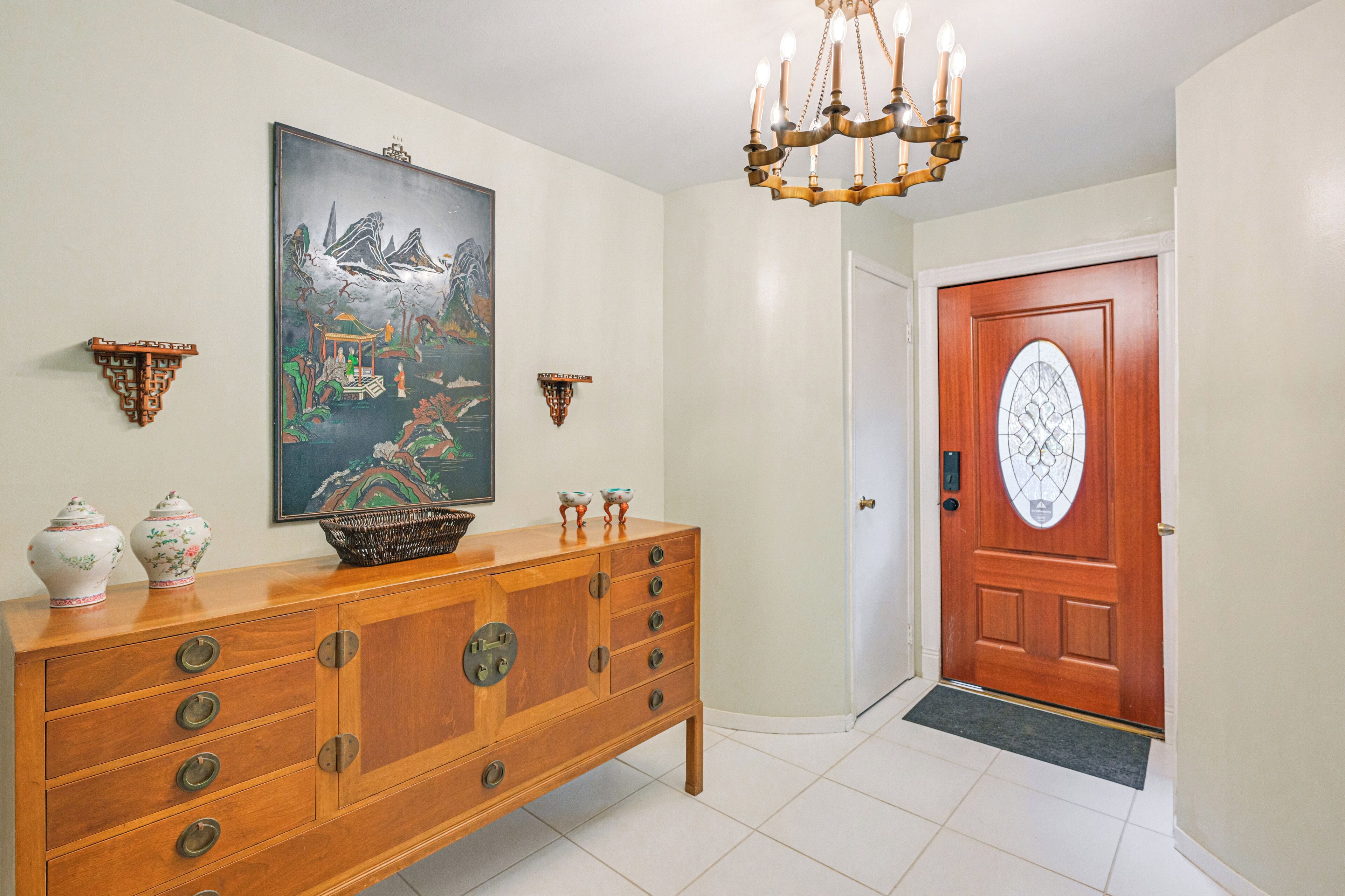 Un couloir avec une armoire en bois, un tableau, un lustre et une porte en bois.