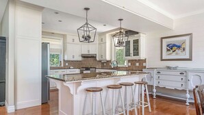 Una cocina con isla central, armarios blancos y una lámpara colgante.