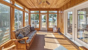 Una habitación amplia con techo de madera, ventanas grandes, ventilador de techo, un sofá y vistas al exterior.