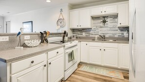 Une cuisine moderne avec des meubles blancs, un plan de travail en granit, une cuisinière et un pare-feu orné de carreaux gris.