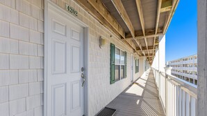 Une terrasse en bois couverte, avec une porte blanche portant l’inscription « 402 » et un paillasson en métal.