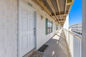 Une terrasse en bois couverte, avec une porte blanche portant l’inscription « 402 » et un paillasson en métal.