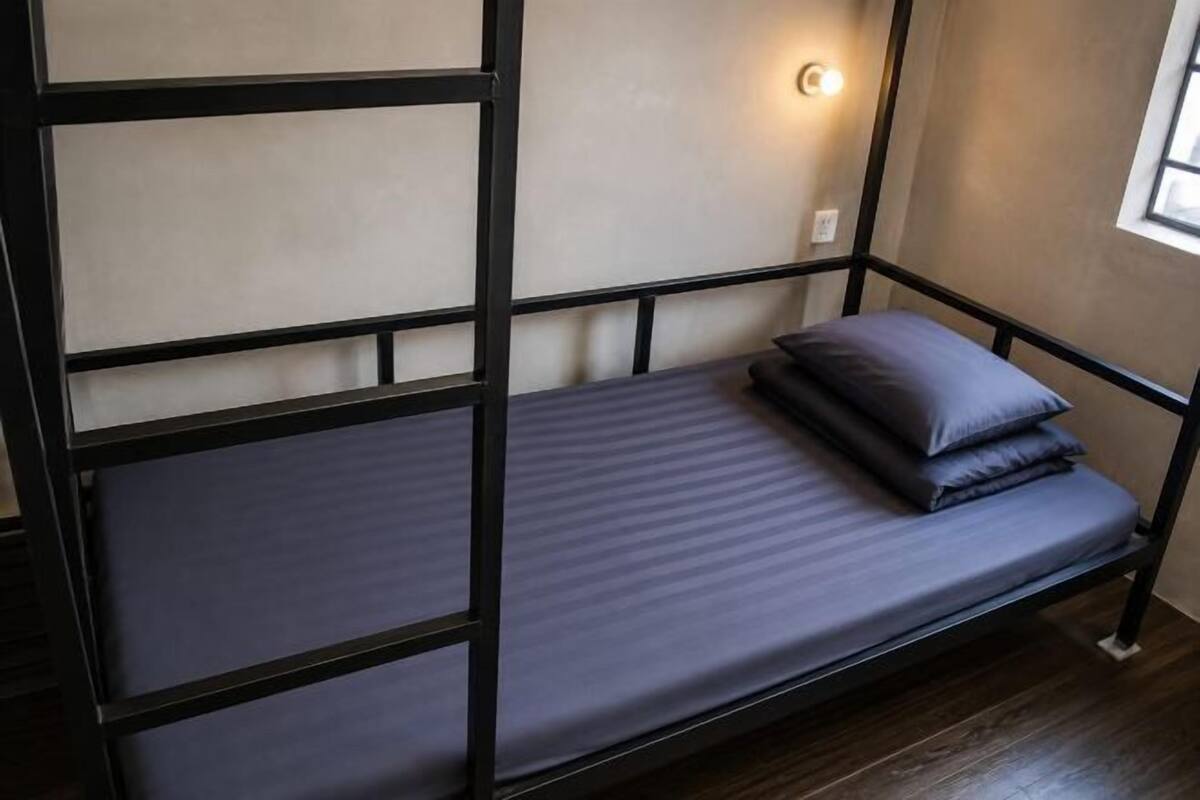A bunk bed with a mattress and pillows, a wall-mounted light, and a window.