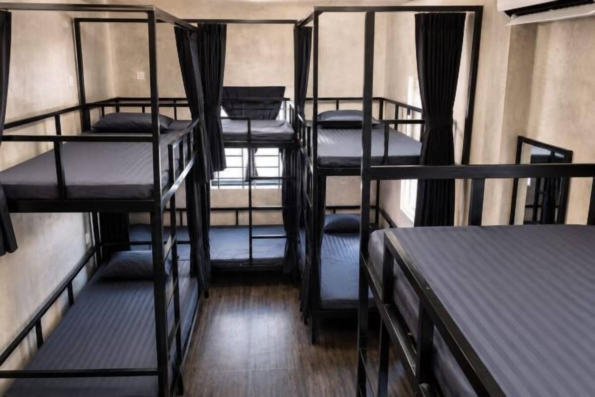 A bunk room with multiple beds, curtains, and a window.