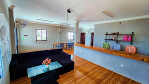 A spacious room with a black sofa, a glass coffee table, a wooden reception desk, and a wall-mounted shelf with items. - The Drop Inn (Siem Reap)