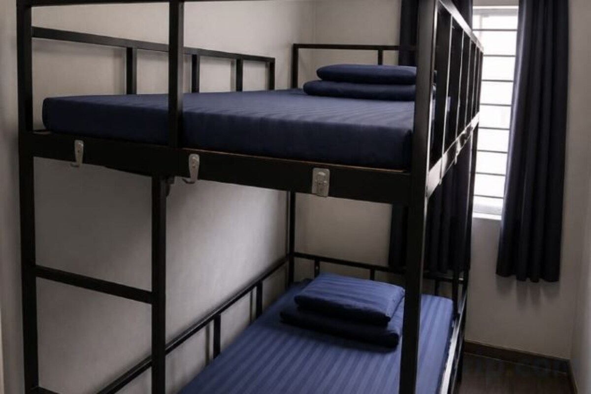 A bunk bed with a mattress and pillows, a window with curtains, and a wall-mounted light fixture.