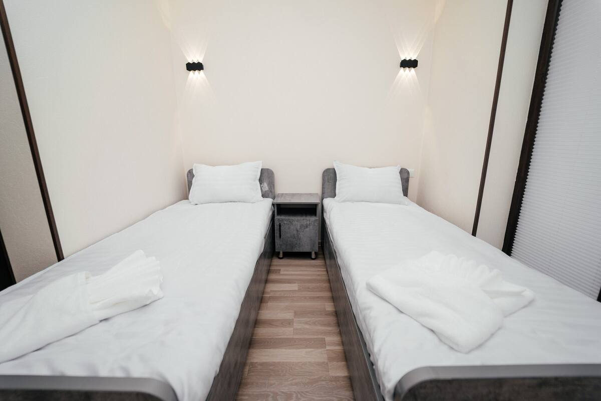 Ein Doppelzimmer mit zwei Einzelbetten, einem kleinen Nachttisch und einem Nachtschränkchen.