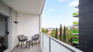 A balcony with two chairs and a table, a glass door, and a view of buildings and trees. - Lakeside 1-Bed with A/C, Parking & Balcony (Greenway)