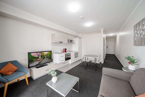 Una sala de estar moderna con una televisión de pantalla plana, un sofá, una mesa de centro y un comedor con una mesita y sillas.