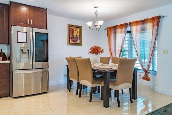 Une cuisine moderne avec un réfrigérateur en acier inoxydable, une table à manger avec six chaises et un lustre.