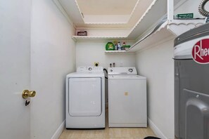 Un lavadero con dos lavadoras blancas, un estante con productos de limpieza y una puerta con pomo de latón.