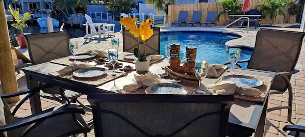 Una mesa de comedor preparada para dos personas con temática tropical, que incluye decoraciones tiki y una planta pequeña.