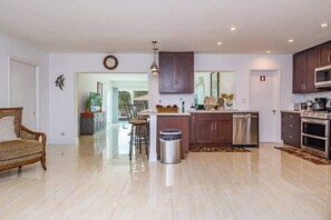 A spacious living room with a sofa, a dining area with chairs, a kitchen with modern appliances, and a large window.