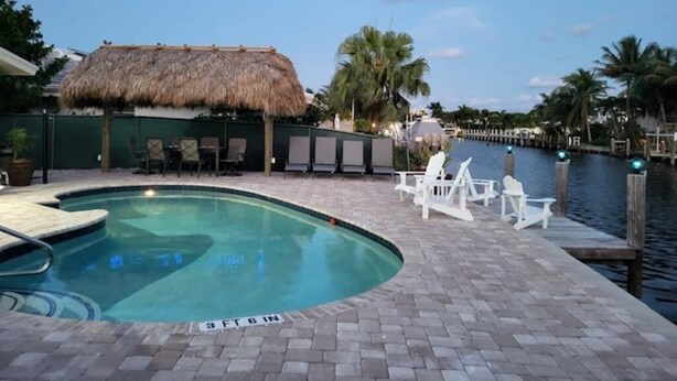 A swimming pool with a thatched roof structure, lounge chairs, and a dock extending into a body of water. - Diana's Waterfront Villa (Fort Lauderdale)