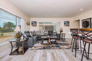 A modern living room with a sectional sofa, a coffee table, and a dining area with bar stools.