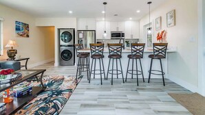 A modern kitchen with white cabinets, a central island with bar stools, a washing machine, and a microwave. - Diana's Waterfront Villa (Fort Lauderdale)