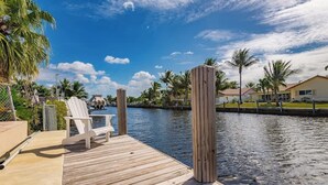 A wooden dock with white chairs, a calm water body, and palm trees in the background. - Diana's Waterfront Villa (Fort Lauderdale)
