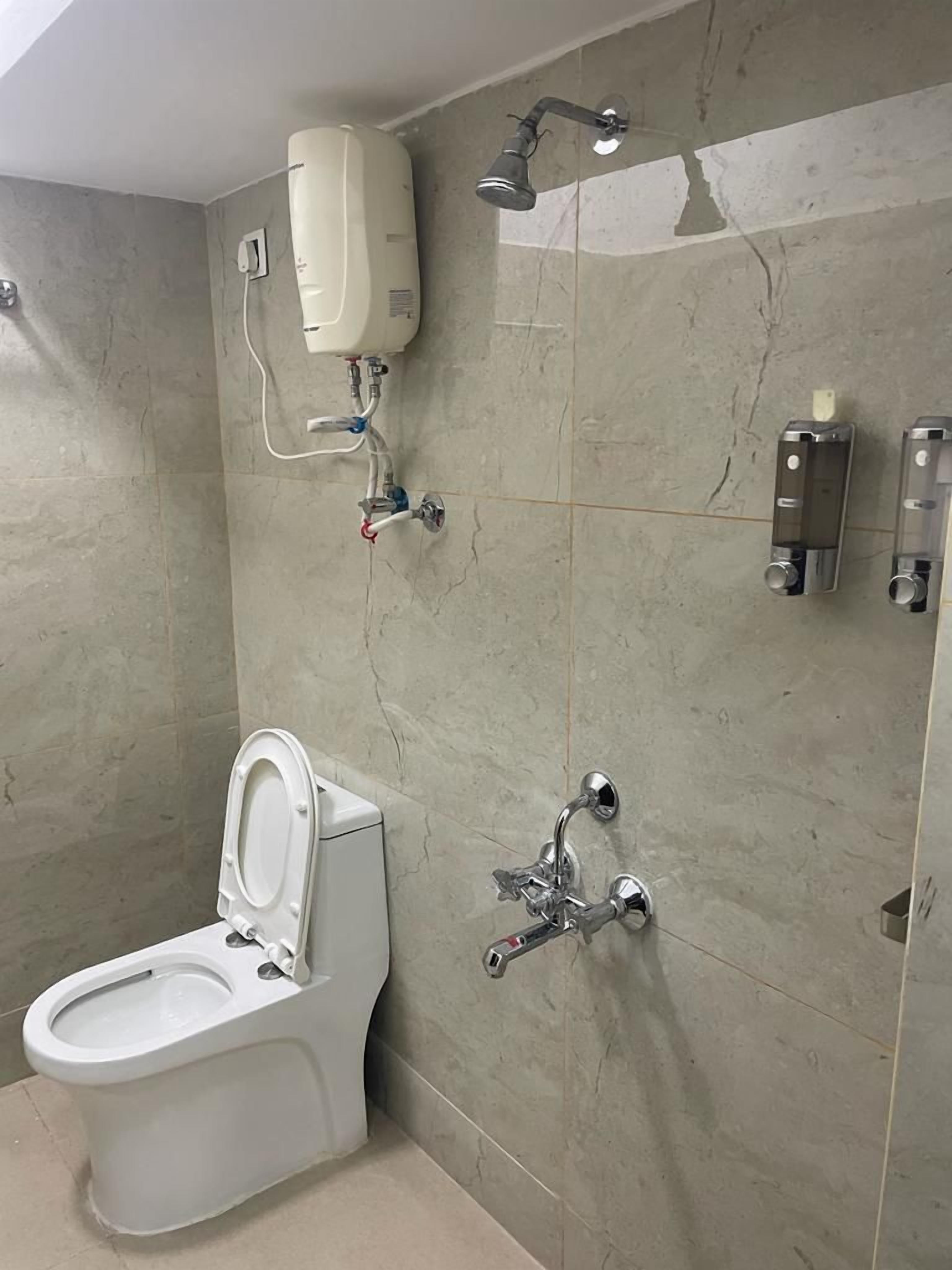 A bathroom with a toilet, a wall-mounted shower, and a hand dryer.