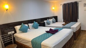 A hotel room with two beds, each with a headboard, white bedding, teal and blue pillows, and a teal quilted runner. - SMJ GRAND HOTEL & MAHAL (Madurantakam)