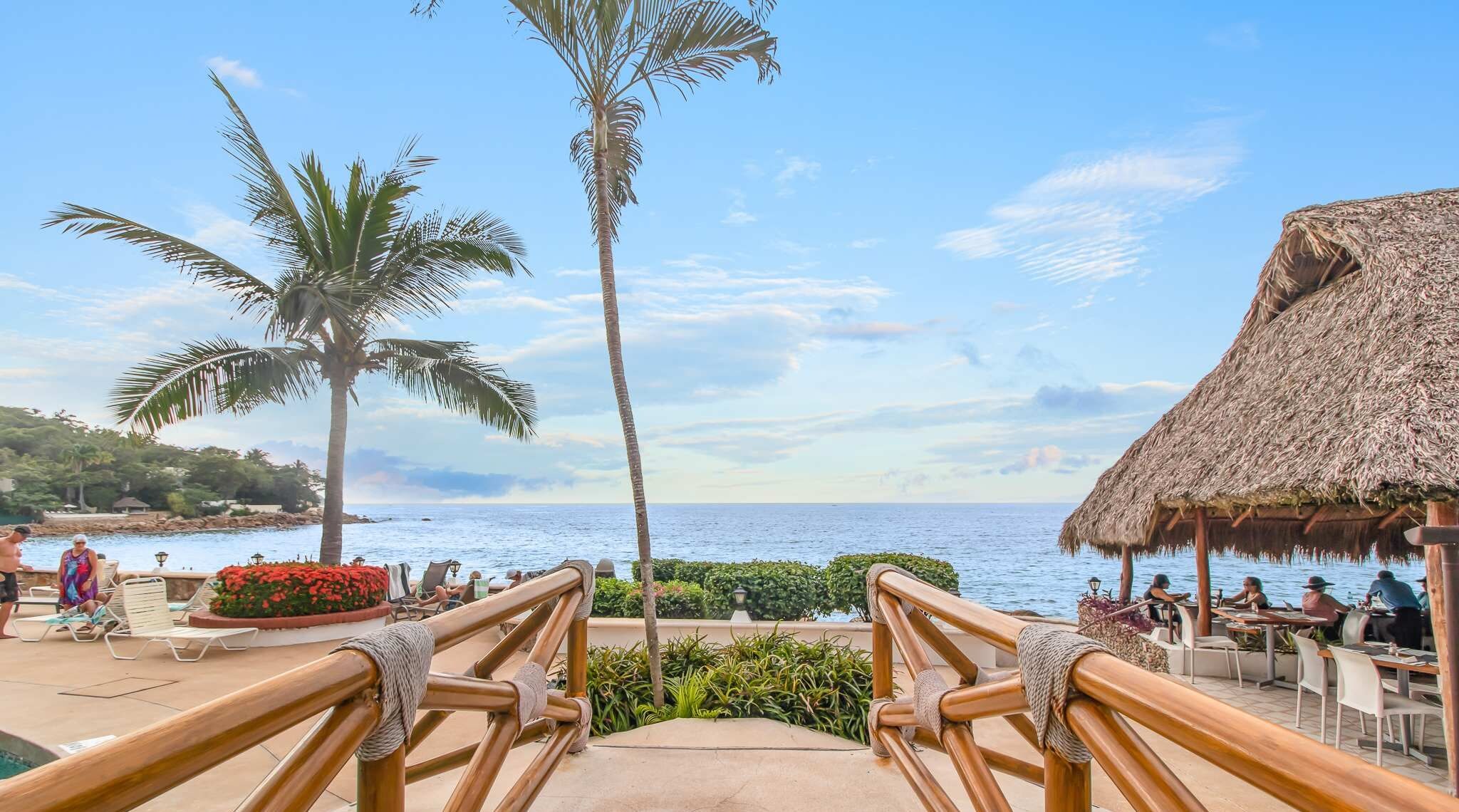 Un resort con piscina, palmeras y una estructura de techo de paja.