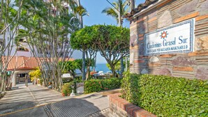 A stone wall with a sign for 'Condominios Girasol Sur' and a view of a coastal area with palm trees and a building with a red roof.