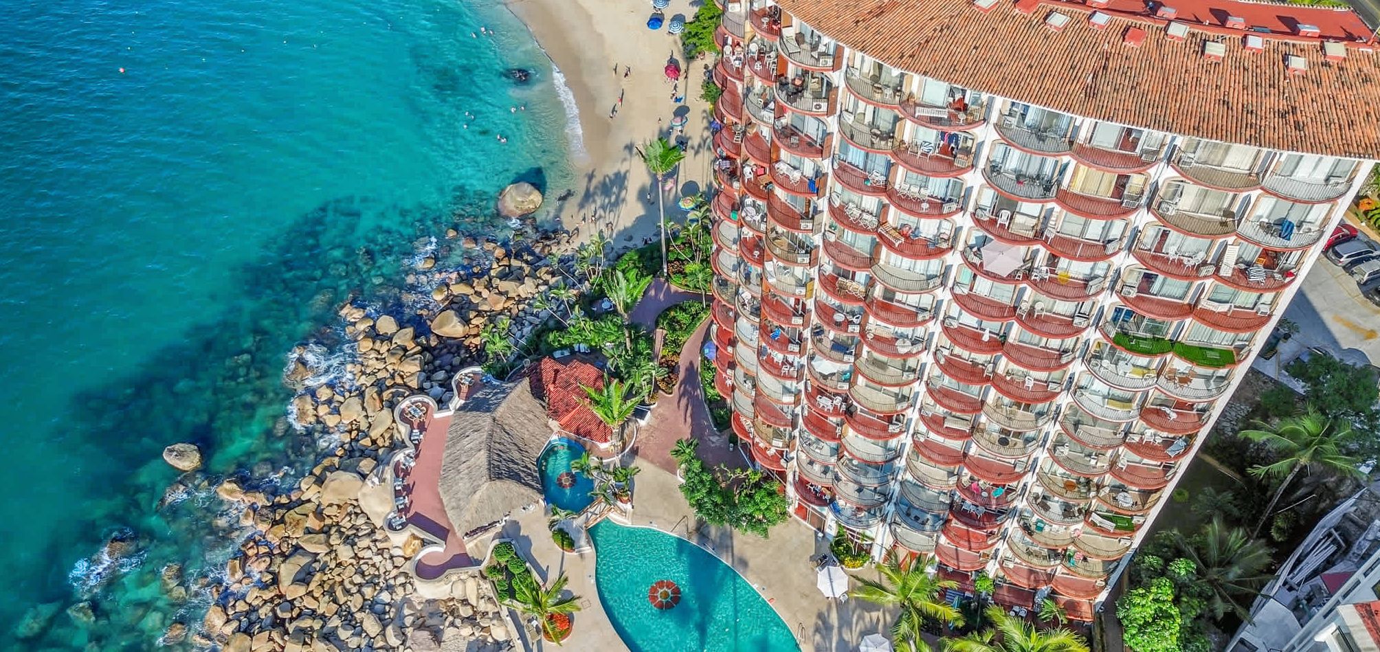 A high-rise hotel with multiple balconies, a pool area, and a beachside location.