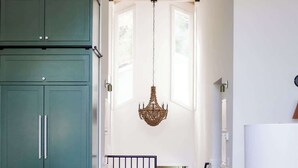 Een keuken met blauwgroene kastjes, een houten eettafel en stoelen. Er hangt een kroonluchter aan het plafond.