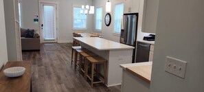 Une cuisine moderne dotée d’un îlot central, de tabourets en bois, d’un four encastré et d’un réfrigérateur.