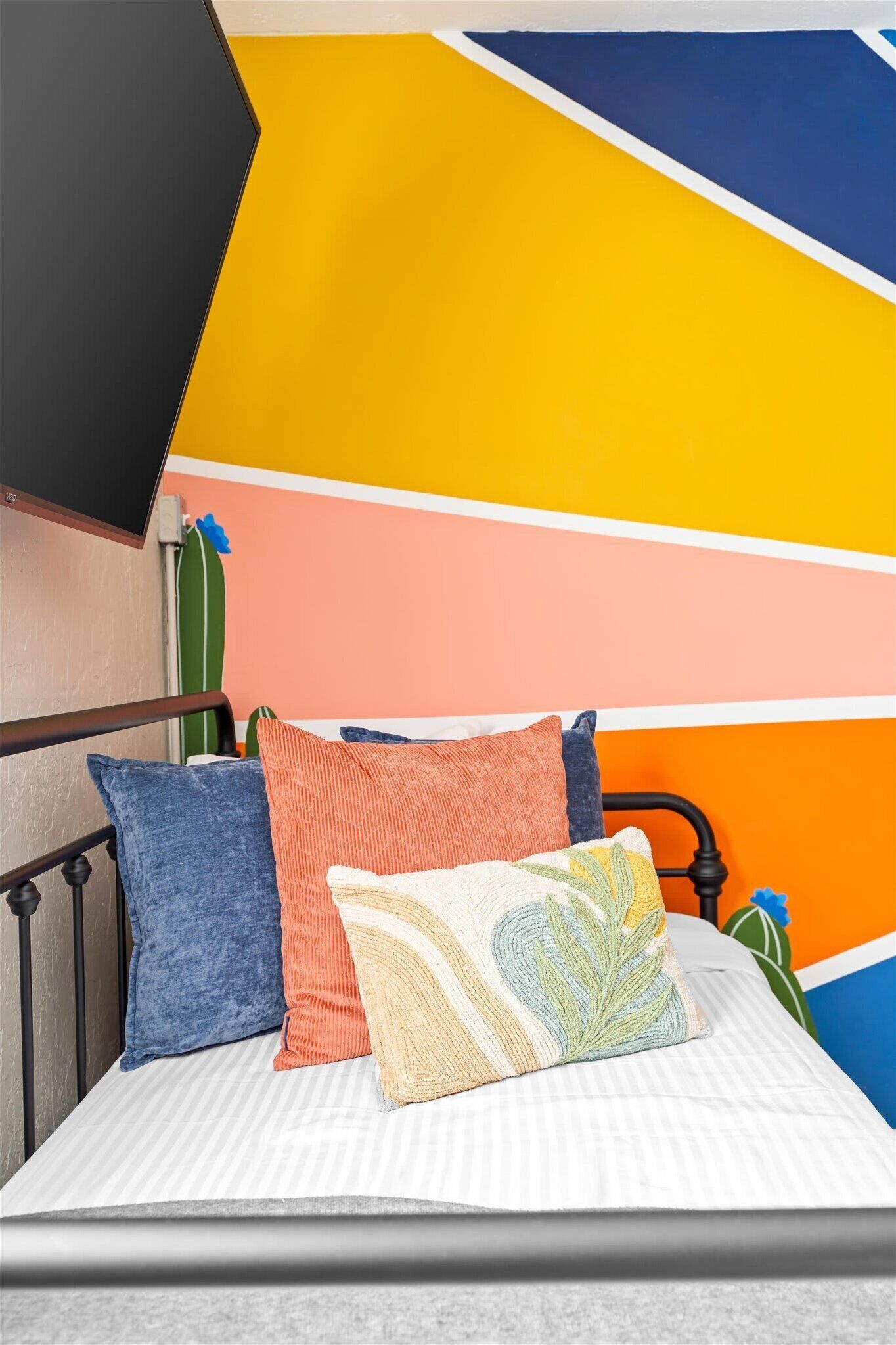 A bed with a striped bedspread, a black metal headboard, and colorful pillows.