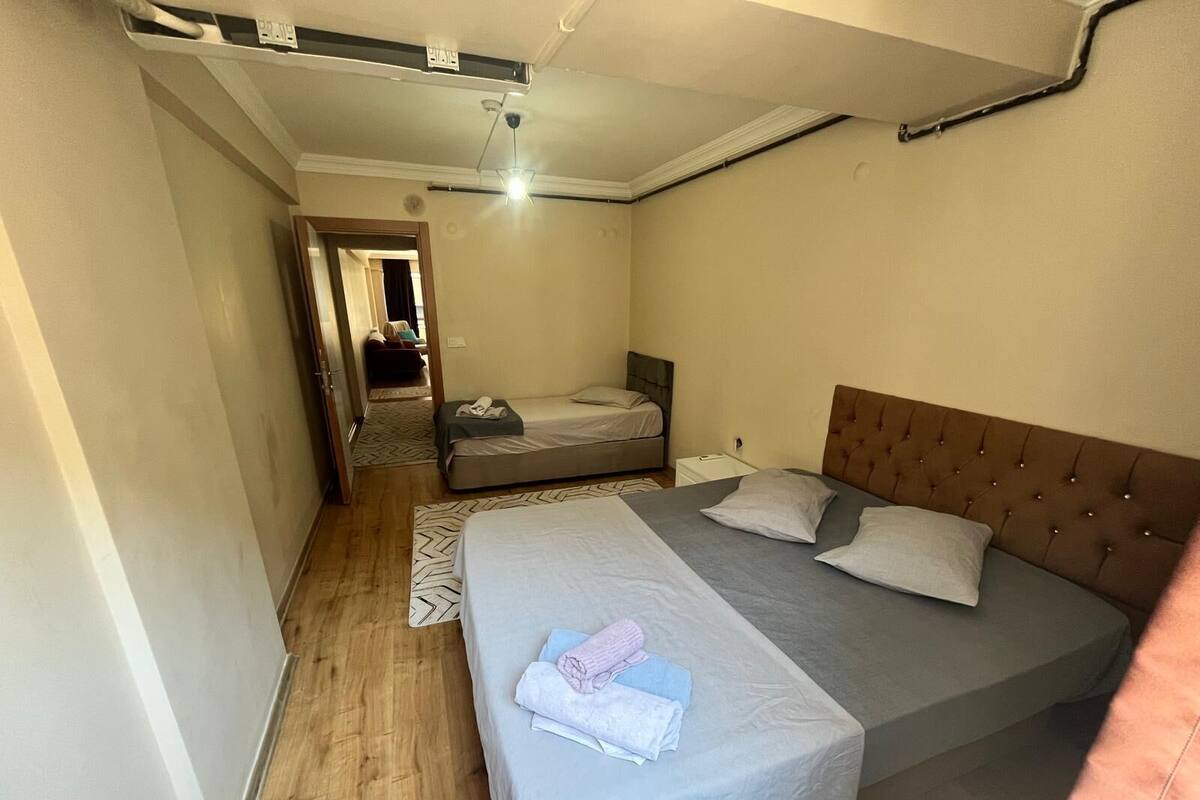 A bedroom with two beds, a wooden floor, a ceiling fan, and a visible door leading to another room.