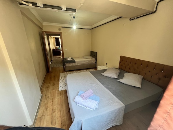 Un dormitorio con dos camas, suelo de madera, ventilador de techo y una puerta visible que da a otra habitación.