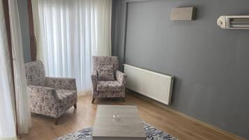A living room with two floral armchairs, a small coffee table, a radiator, and a window with sheer curtains.