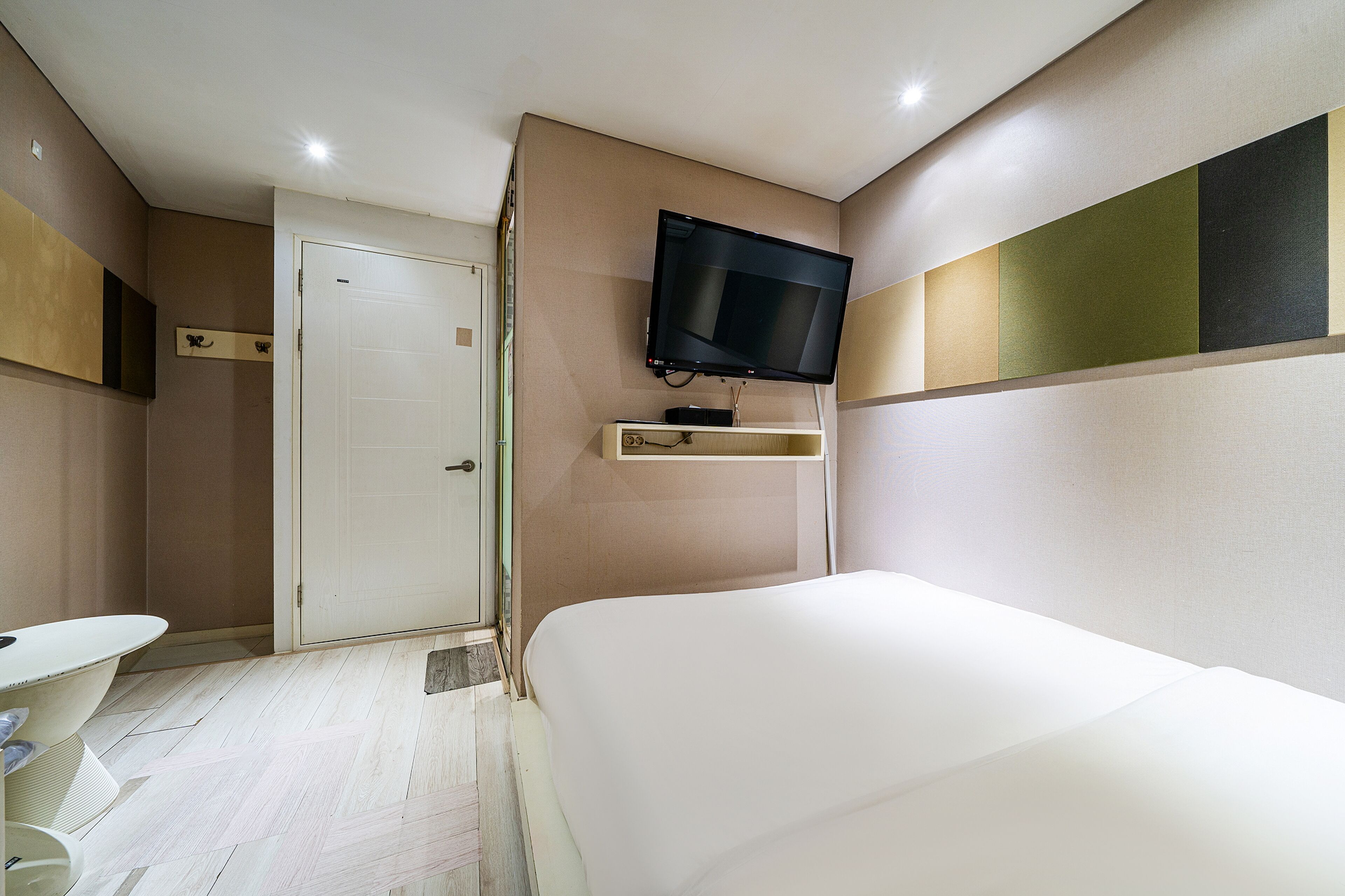 Een hotelkamer met een bed, een aan de muur bevestigde televisie, een deur en een klein tafeltje.