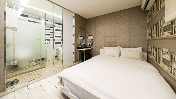 A modern hotel room with a large bed, a glass shower enclosure, a small bedside table, and a wall-mounted air conditioning unit. - Hotel INN Seoul (Seoul)