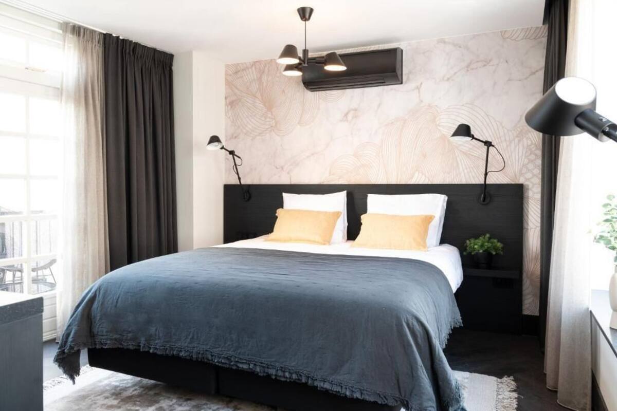Ein modernes Schlafzimmer mit einem großen Bett, zwei Nachttischlampen, einer Decken-Klimaanlage und Blick auf einen Balkon.