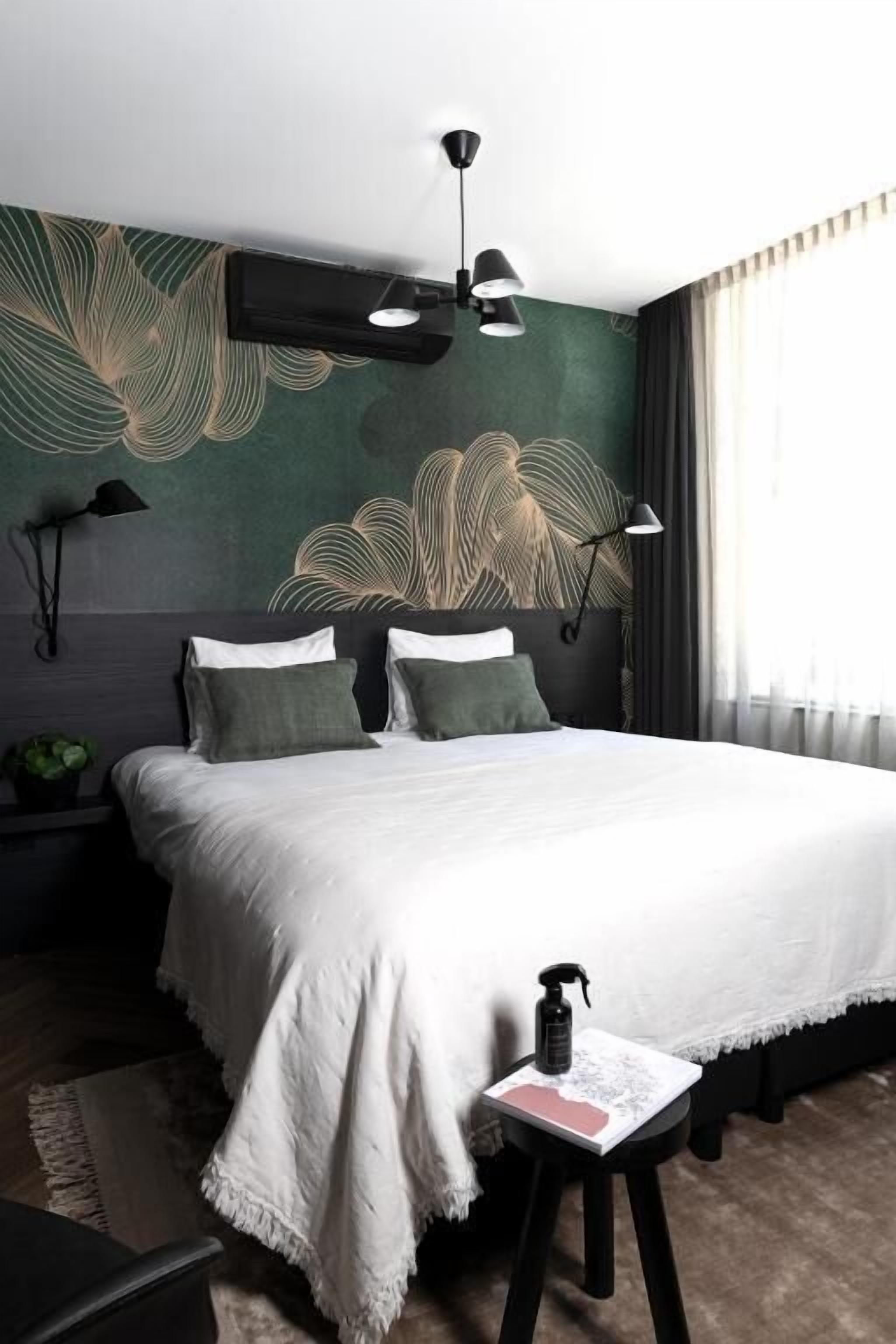 A modern bedroom with a large bed, a wall mural, and a bedside table with a book and a bottle.