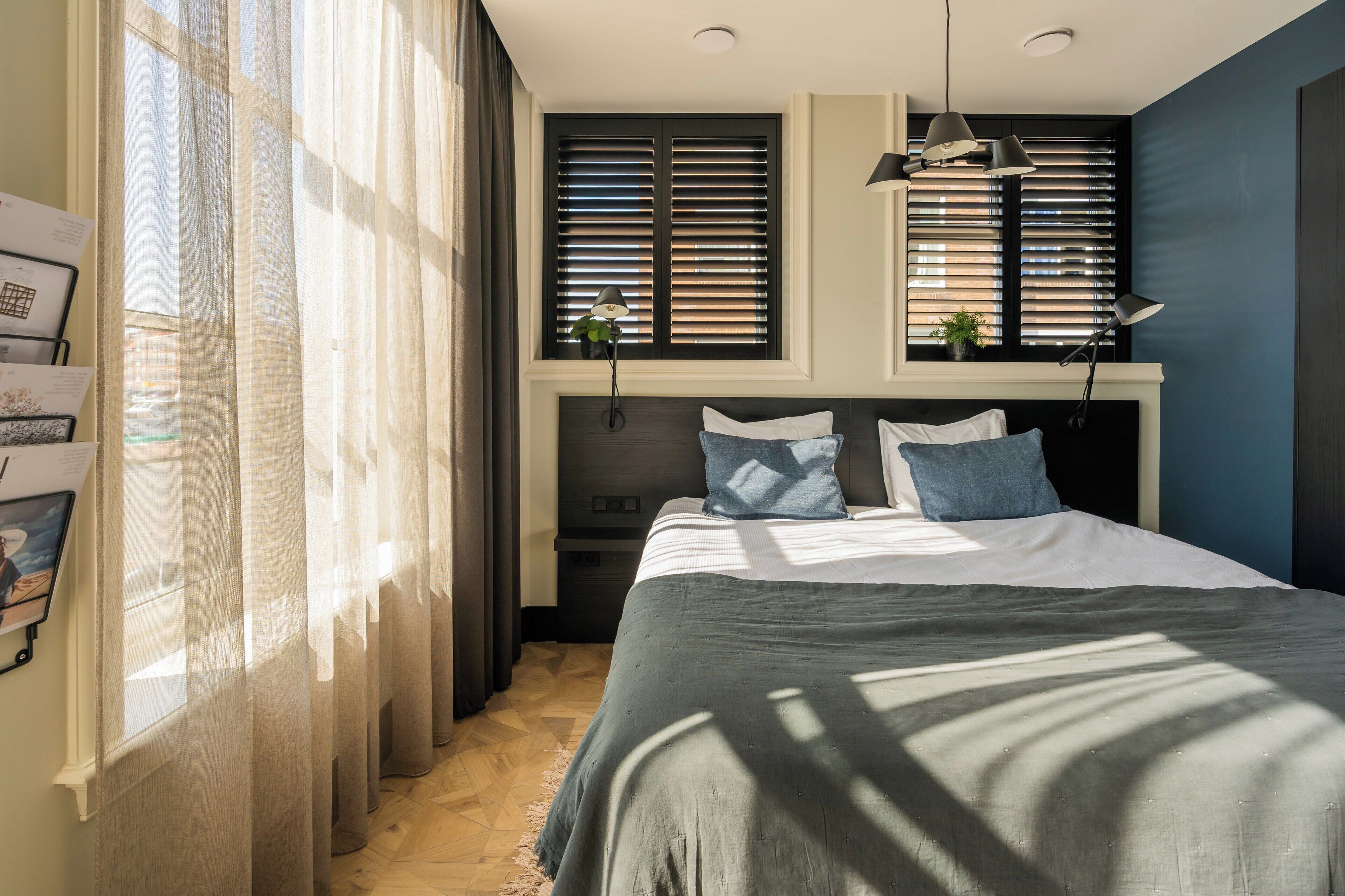 Un dormitorio con una cama, una ventana con persianas, una lámpara y una planta en el alféizar.