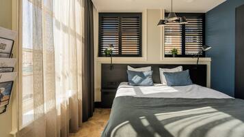 Un dormitorio con una cama, una ventana con persianas, una lámpara y una planta en el alféizar.