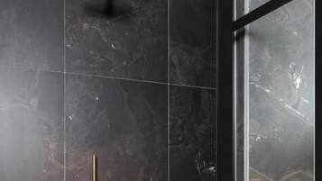 Ducha moderna con cabezal de ducha dorado y cabezal de ducha de mano, sobre baldosas de mármol oscuro.