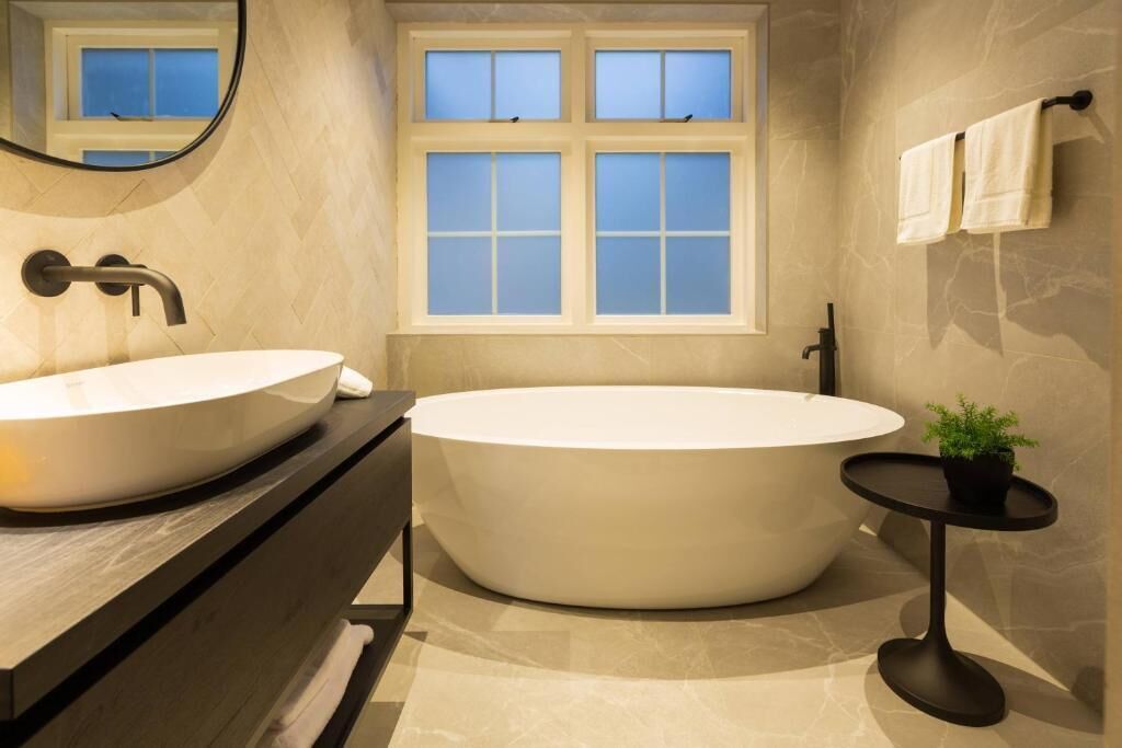 A modern bathroom with a freestanding bathtub, a round sink, and a small round table with a plant.