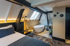 Une chambre moderne avec une lucarne, un grand lit, une baignoire et un fauteuil.
