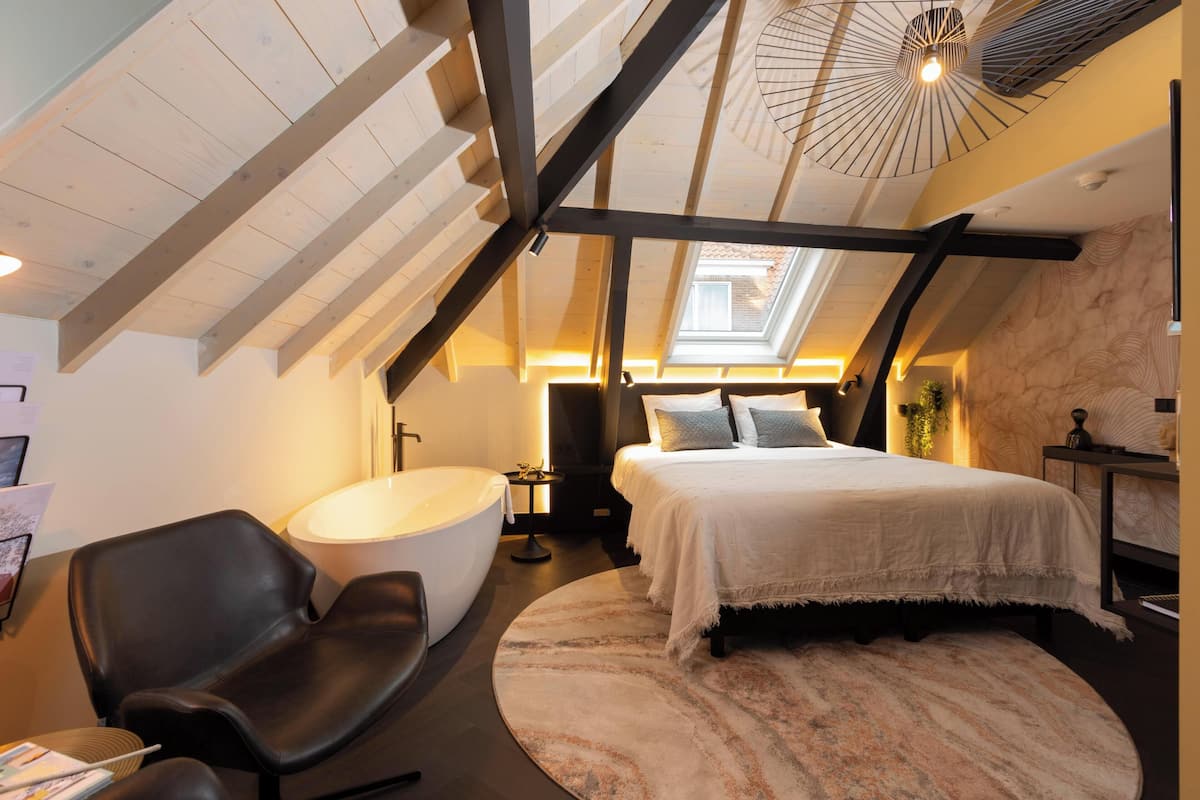 Ein modernes Schlafzimmer mit Oberlicht, einem großen Bett, einer Badewanne und einem Ledersessel.