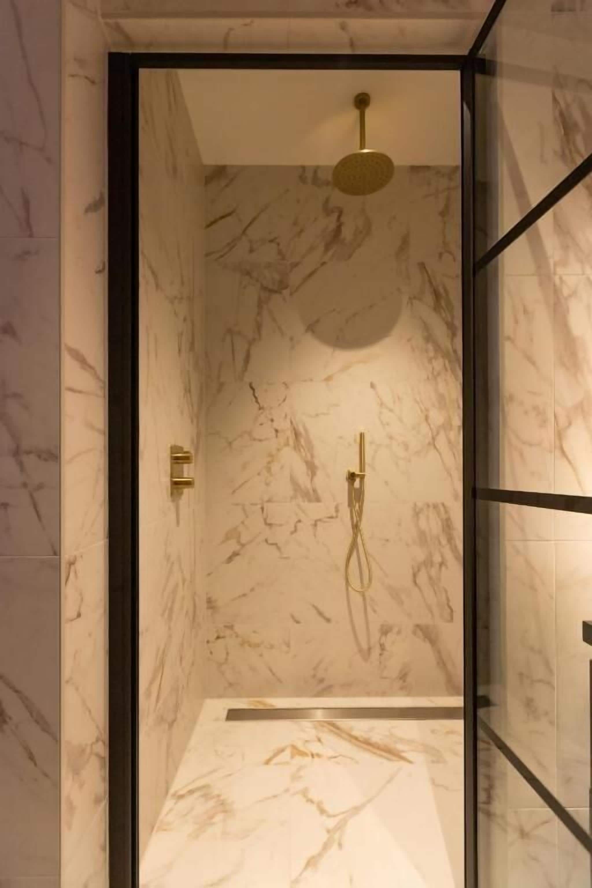 Eine moderne Dusche mit Marmorwänden und einer Glasabtrennung.