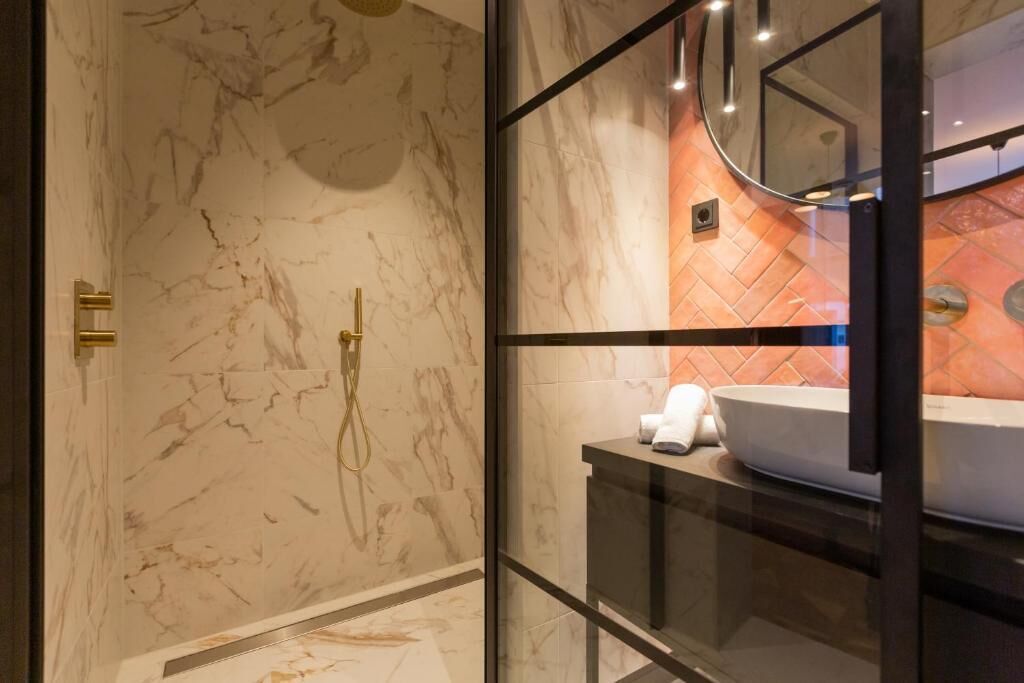 Un baño moderno con paredes de mármol, cabina de ducha de vidrio y lavamanos con espejo.