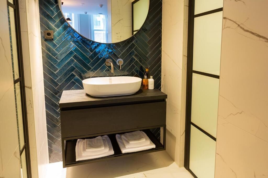 Une salle de bain moderne avec un grand lavabo ovale, un miroir au-dessus et un pare-éclaboussures à motifs en chevrons. Deux serviettes blanches sont pliées et posées sur une étagère située sous le lavabo.