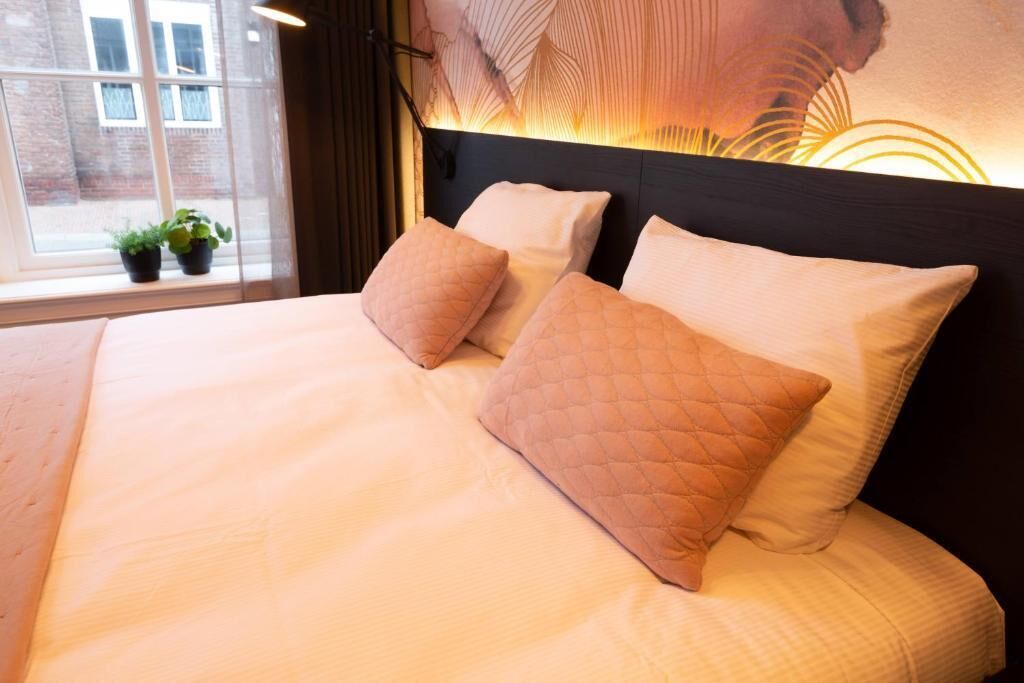Un lit bien fait, avec un oreiller matelassé et une tête de lit dotée d’un luminaire.