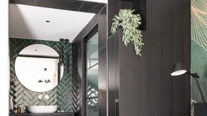 Une salle de bain moderne avec un miroir rond, un lambris en bois foncé et une plante verte en guise de décoration.