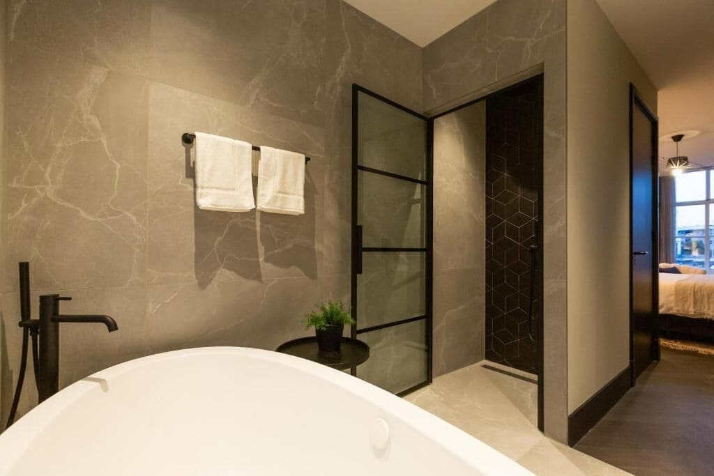 A modern bathroom with a freestanding bathtub, a glass shower enclosure, and a potted plant on a small table.