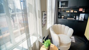 Une cuisine moderne avec des meubles de couleur sombre, une table ronde en bois agrémentée d’une plante en pot et un fauteuil blanc placé près d’une fenêtre ornée de rideaux légers.