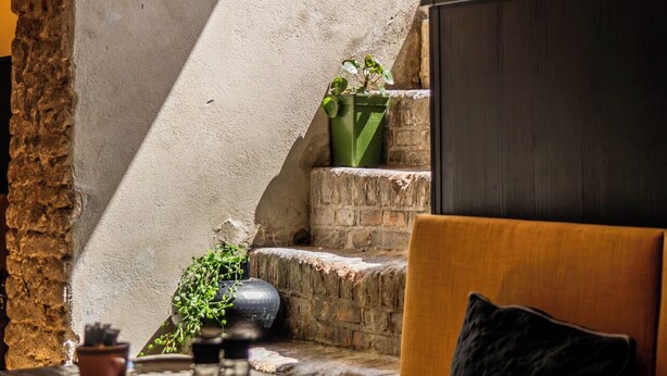Un coin repas agrémenté d’un mur en pierre rustique, d’un escalier en bois et d’un canapé moderne.